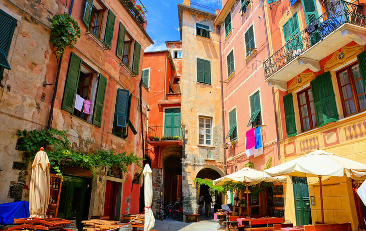 Malebunte Häuser und Cafés auf einem sonnigen Platz in Italien.