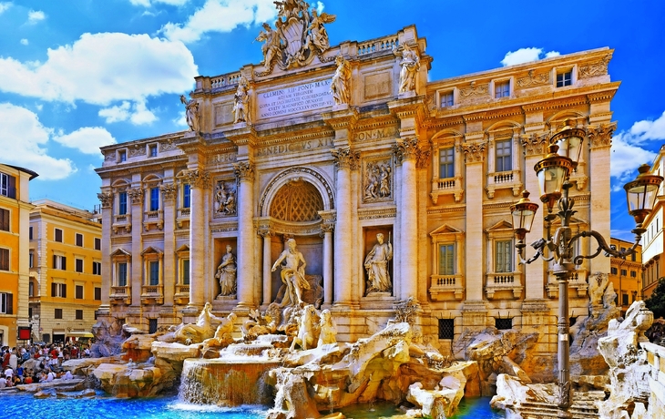 Brunnen vor einem barocken Palast mit Statuen und blauem Himmel.