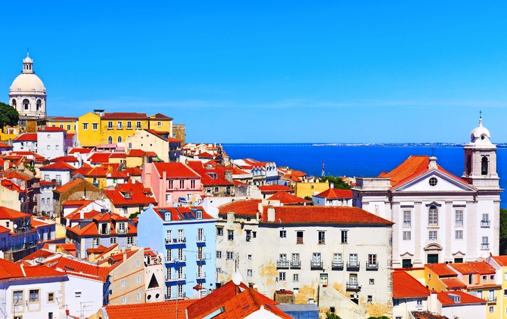 Bunte Dächer und Gebäude in Lissabon mit Blick auf das Meer.