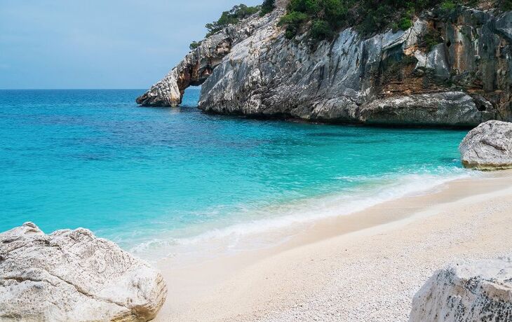 Türkise Bucht mit Sandstrand und Felsen im Hintergrund.