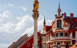 Statue auf Säule vor historischen Gebäuden und Himmel mit Wolken.