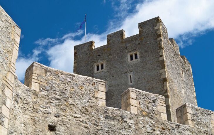 Mittelalterliche Steinburg mit Zinnen vor blauem Himmel.