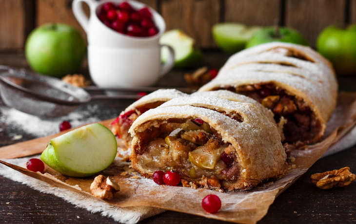 Apfelstrudel mit Nüssen, Preiselbeeren und Apfelscheiben auf Holztisch.