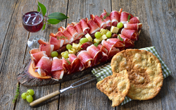 Antipasti-Platte mit Schinken, Melone und Brot auf Holztisch.