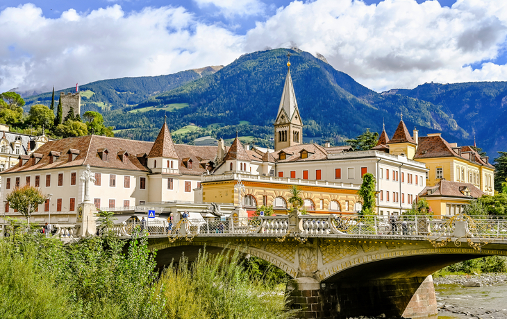 Historische Gebäude und Brücke vor Bergkulisse in Meran, Italien.