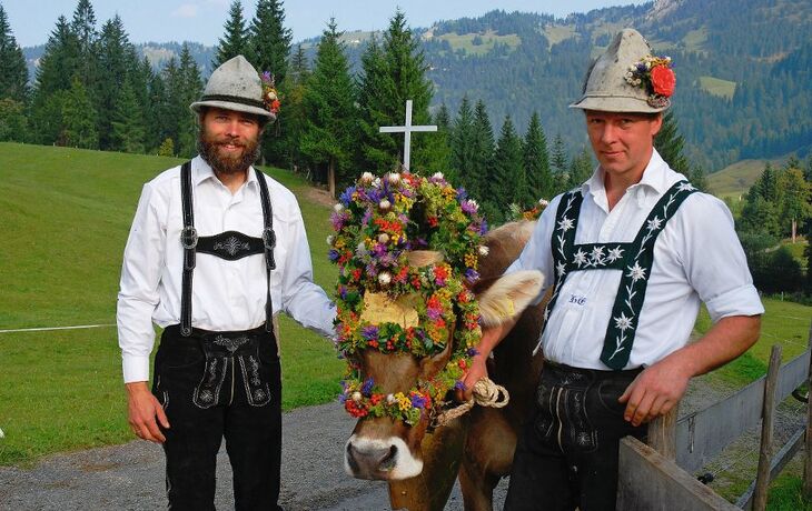 Zwei Männer in Tracht beim Almabtrieb mit geschmückter Kuh in Balderschwang.
