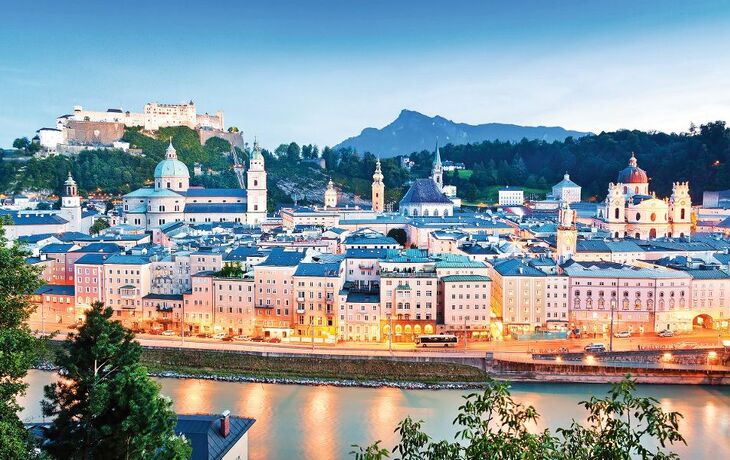 Blick auf Salzburg bei Abenddämmerung mit Festung und Kirchtürmen.