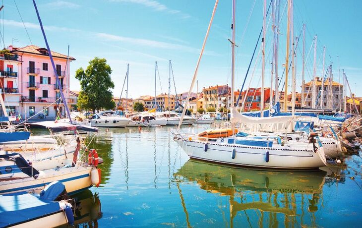 Yachthafen mit mehreren Segelbooten im Wasser, umgeben von bunten Gebäuden und blauem Himmel.