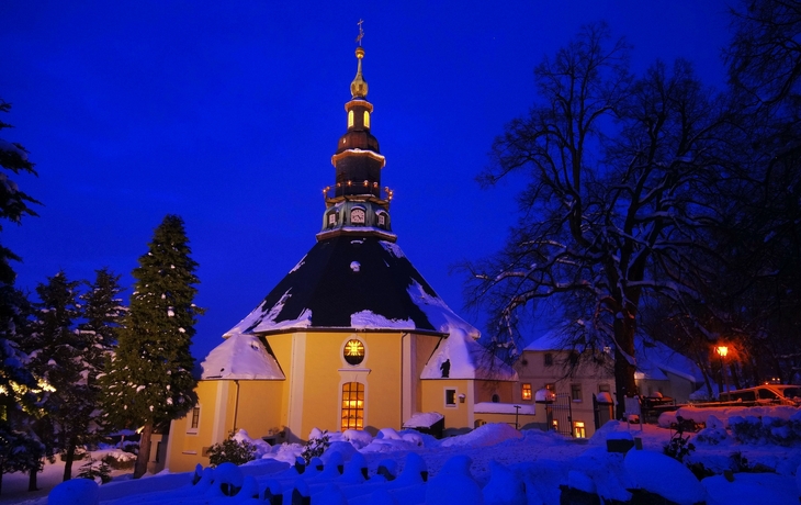Barockkirche im Schnee bei Nacht, beleuchtet von warmen Lichtern.