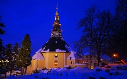 Barockkirche im Schnee bei Nacht, beleuchtet von warmen Lichtern.