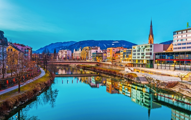 Uferpromenade einer Stadt mit bunten Gebäuden und Bergblick bei Abenddämmerung.