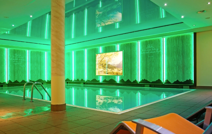 Hallenbad mit grüner Beleuchtung und Liegestühlen am Rand.