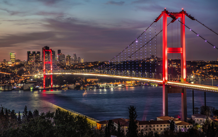 Brücke über einem Fluss bei Sonnenuntergang mit Stadt im Hintergrund.