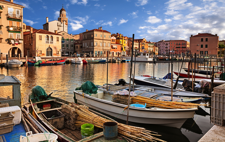 Hafen mit Booten und bunten Gebäuden im Hintergrund bei Sonnenschein.