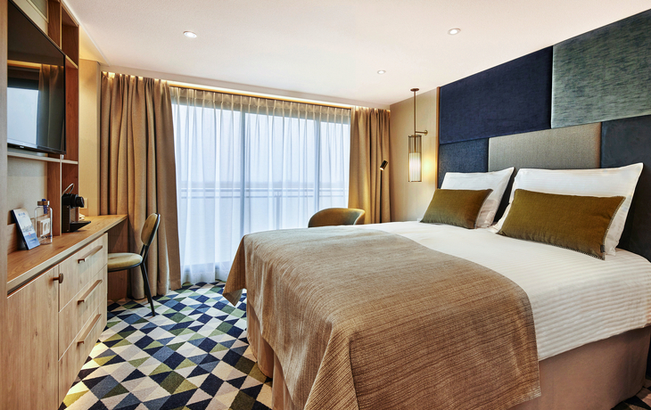 Moderner Kabinenbalkon mit Bett, Schreibtisch und Fenster auf einem Kreuzfahrtschiff