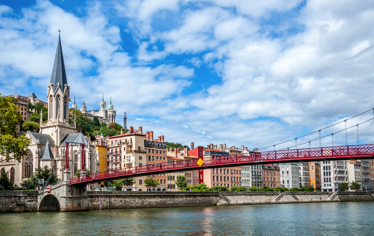 Flussansicht mit einer Kirche, einer roten Brücke und bunten Gebäuden im Hintergrund.