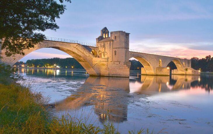 Mittelalterliche Steinbrücke über einen ruhigen Fluss im Sonnenuntergang.