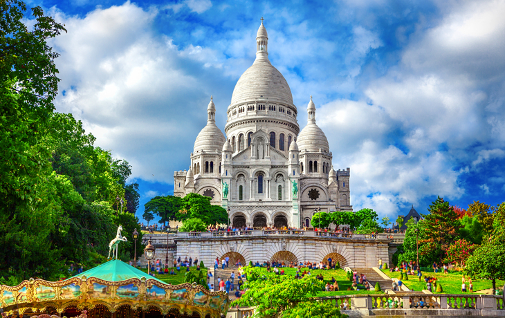 Blick auf die Basilika Sacré-Cœur in Paris, mit Karussell im Vordergrund.