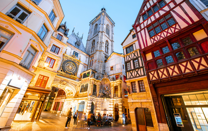 Fachwerkhäuser und historische Uhren in einer Altstadt bei Dämmerung.